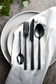 a white plate topped with silverware on top of a cloth covered table next to utensils