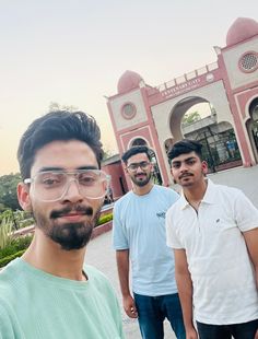 three men are standing in front of a pink building with arches and arched doorways