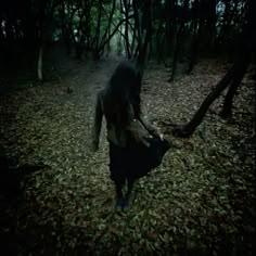 a woman walking through the woods with leaves all over her and holding an object in her hand