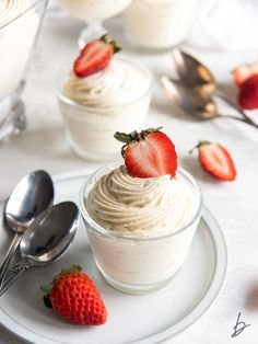 two desserts with whipped cream and strawberries on a plate next to spoons