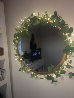 a mirror that has some plants on it and lights around the frame in front of it