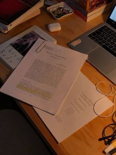 an open laptop computer sitting on top of a wooden desk next to papers and headphones