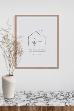 a white vase sitting on top of a marble counter next to a framed print with a house