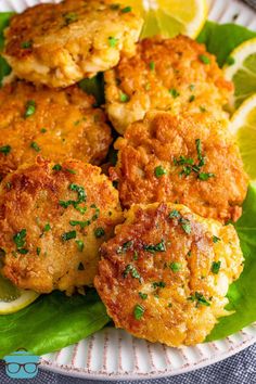 some crab cakes are on a plate with lemon wedges and green leafy greens