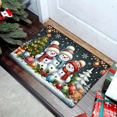 a door mat with three snowmen on it next to christmas presents and a tree