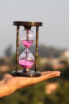 a hand holding an hourglass with pink sand