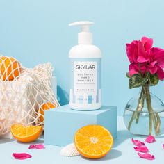 a bottle of soap sitting on top of a table next to oranges and flowers