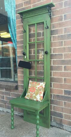 a green bench sitting next to a window on the side of a brick building in front of a store