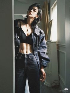 a woman standing in front of a door wearing jeans and a crop top with her hands on her hips