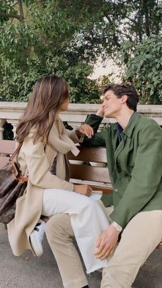 a young man and woman sitting on a bench talking to each other in the park