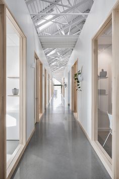 an empty long hallway with wooden doors and white walls on both sides is lit by daylight