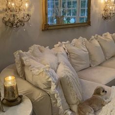 a dog laying on top of a white couch next to pillows and a table with candles