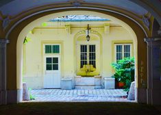 an archway leading into a yellow building with potted plants on either side and two white doors