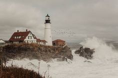 a lighthouse on top of a cliff with waves crashing in front of it and birds flying around