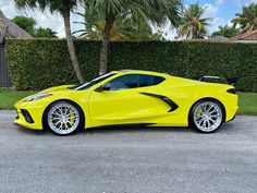 the yellow sports car is parked in front of some bushes and palm tree's