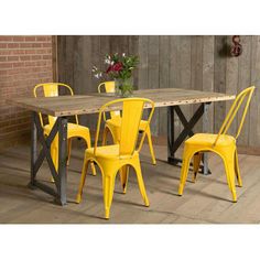 a dining room table with yellow chairs next to a brick wall and wooden plank floor