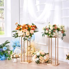 three gold vases filled with flowers on top of a wooden floor next to a window