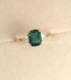 an emerald and diamond ring sitting on top of a white cloth