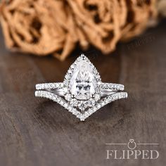 an engagement ring with a pear shaped diamond center surrounded by pave diamonds on a wooden surface