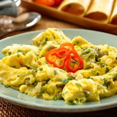 an omelet with tomatoes and green onions on a blue plate next to bread