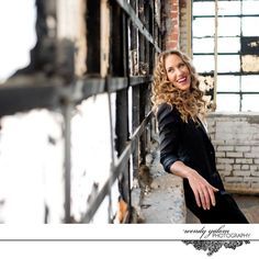 a woman leaning against a brick wall in an old building smiling at the camera with her hands on her hips