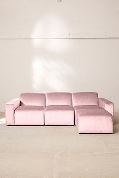 a pink couch sitting on top of a floor next to a white wall in an empty room