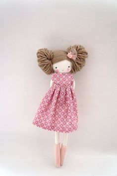 a doll with brown hair wearing a pink dress and pink booties, standing against a white background