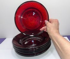 a stack of red glass plates being held by a person's hand over them