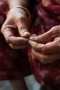 an old woman holding something in her hands with one hand and the other another's thumb