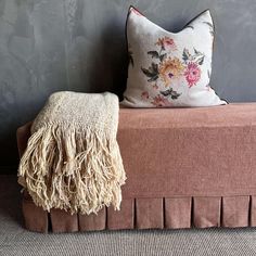 a brown bench sitting next to a wall with a flowered pillow on top of it