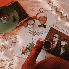 a woman holding a cup of coffee next to some records and christmas lights on the ground