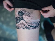 a person with a tattoo on their leg that has an ocean wave coming out of it