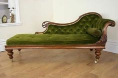 a green couch sitting on top of a hard wood floor next to a white wall