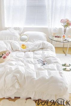 a bed with white comforter and pillows in a bedroom next to a window,