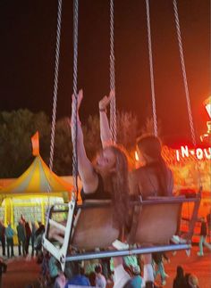 two women sitting on a swing at an amusement park while others watch from the stands