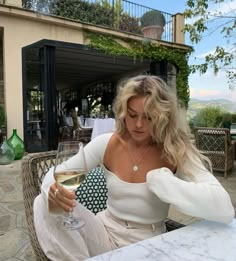 a woman sitting at a table with a glass of wine in her hand and looking down