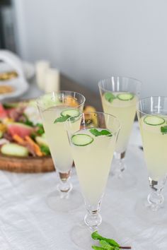 three glasses with cucumber and mint garnish sit on a white table cloth