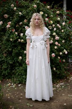 a woman wearing a white dress standing in front of flowers