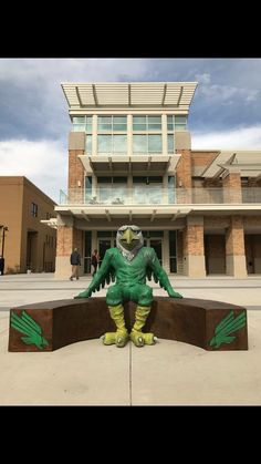 a statue of a green creature sitting on top of a bench in front of a building