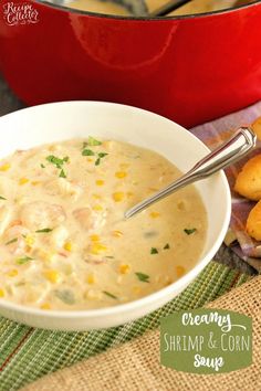 a bowl of creamy shrimp and corn soup on a table with bread rolls in the background