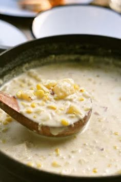 a spoon full of soup with corn on the cob in it and another bowl behind it