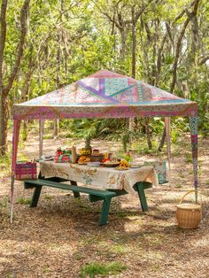 a picnic table under a canopy in the woods with food and drinks set up on it