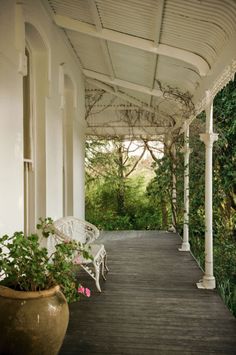 an outdoor covered porch with white furniture and potted plants on the side walk way