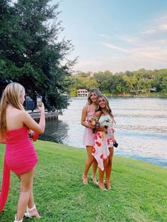 two beautiful women standing next to each other on a lush green field near the water