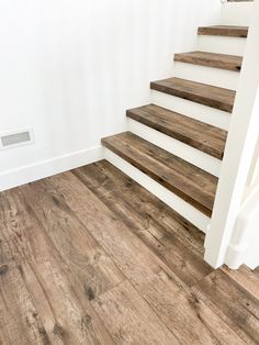 an empty room with wood floors and white walls, stairs leading up to the second floor