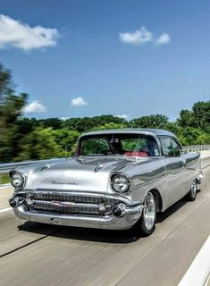 an old silver car driving down the road