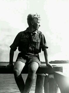 a man sitting on top of a wooden post next to the ocean with his legs crossed