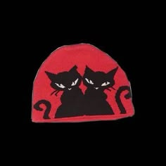 two black cats sitting next to each other on a red and black beanie hat