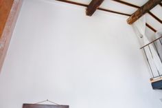 a bed sitting under a wooden beam next to a window in a white walled room