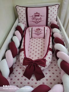 a pink and red baby crib with pillows on the bottom, bow tie around the bumper